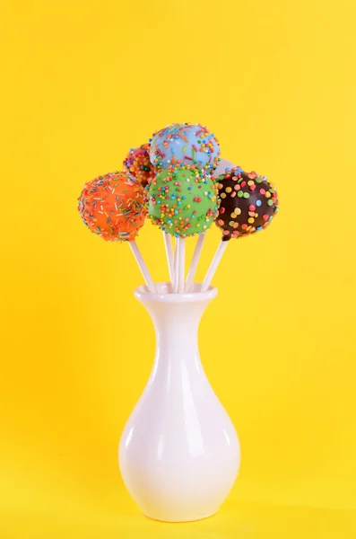 Sweet cake pops in vase on yellow background — Stock Photo, Image