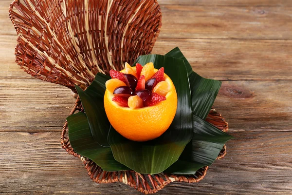 Fruit dessert in orange peel on green leaf on table — Stock Photo, Image