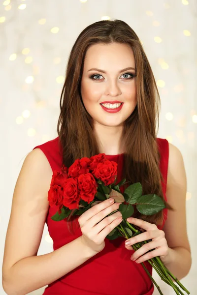 Улыбающаяся девушка с букетом красных роз на фоне огней — стоковое фото