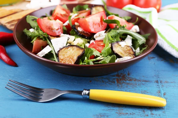 Auberginen-Salat mit Tomaten, Rucola und Feta, auf Serviette, auf farbigem Holzgrund — Stockfoto