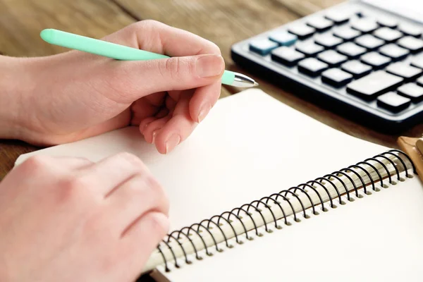 Ręka z długopis, notatnik i kalkulator na drewnianym stole tło — Zdjęcie stockowe