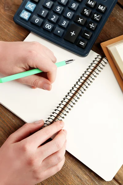 Női kéz, toll, jegyzetfüzet, számológép, fából készült asztal háttér — Stock Fotó