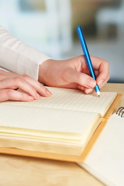 Vrouwelijke hand met pen en dagboek op houten bureaublad op lichte achtergrond Stockfoto