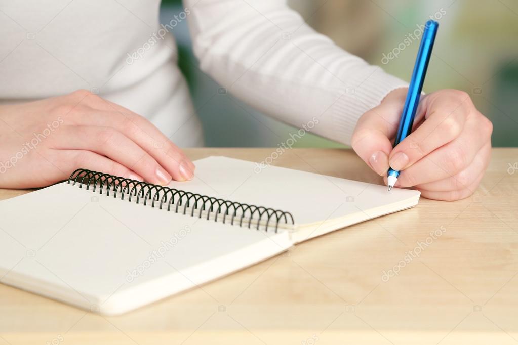 Female hand with pen and notebook at wooden desktop on light background