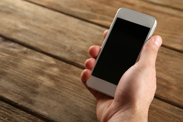 Mano sosteniendo el teléfono móvil inteligente sobre fondo de mesa de madera — Foto de Stock