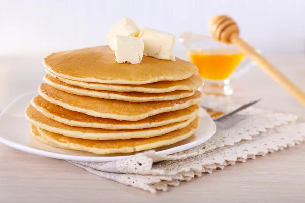 Stack of delicious pancakes with butter and honey in saucer on table and light background — Stock Photo, Image