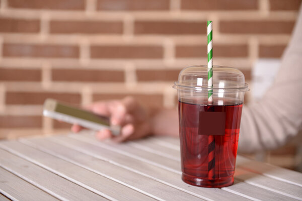 Pomegranate juice in fast food closed cup with tube on wooden table and female hand on brick wall background