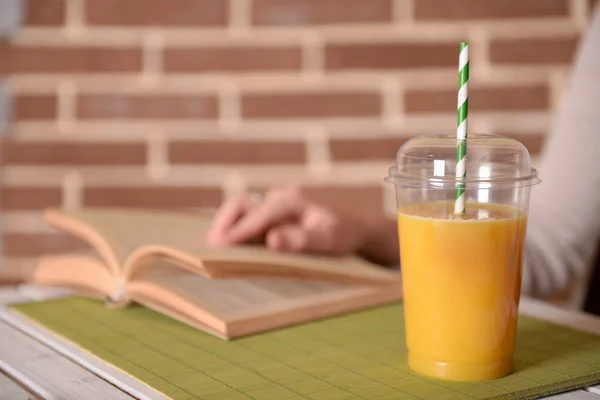 Женская рука за столом с фаст-фудом закрытая чашка апельсинового сока на фоне кирпичной стены — стоковое фото