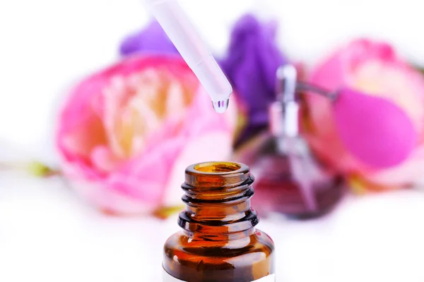 Garrafa conta-gotas de perfume com flores no fundo claro — Fotografia de Stock