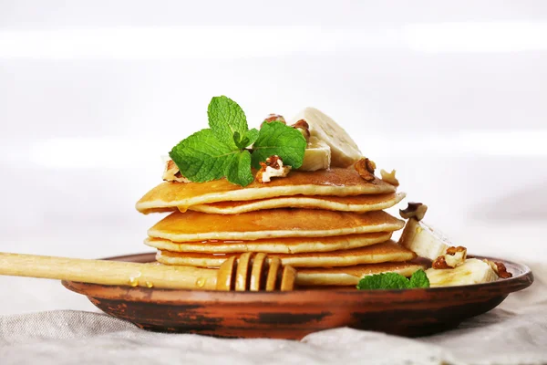 Pila di frittelle con menta, noci e fette di banana sul tavolo con tessuto su tavole di legno sfondo — Foto Stock