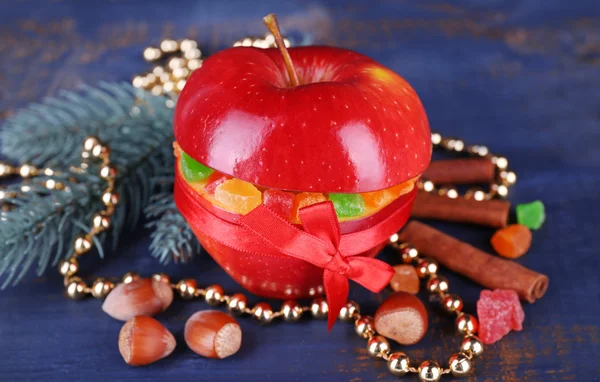 Roter Apfel gefüllt mit getrockneten Früchten mit Zimt, Tannenzweig und Haselnuss auf farbigem Holztischhintergrund — Stockfoto