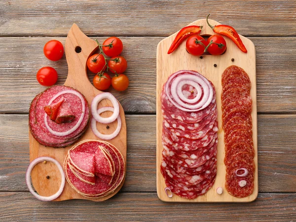 Sliced salami with chili pepper, cherry tomatoes, onion and spices on cutting board and wooden table background — Stock Photo, Image
