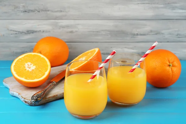 Copo de suco de laranja com palhas e fatias na placa de corte com faca na cor de fundo de madeira — Fotografia de Stock