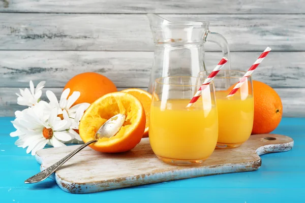 Стекло апельсинового сока с соломинками, ложкой и ломтиками на раскройке доски на фоне цвета дерева — стоковое фото
