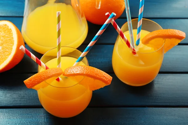 Glass of orange juice with straws and slices on color wooden background — Stock Photo, Image