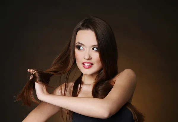 Beautiful young woman with long hair on dark brown background — Stock Photo, Image