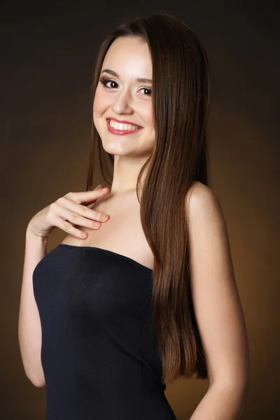 Mooie jonge vrouw met lang haar op donkere bruine achtergrond — Stockfoto