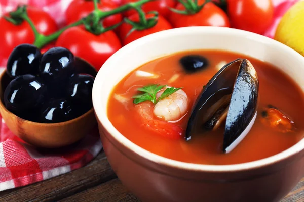 Tasty soup with shrimps, mussels, tomatoes and black olives in bowl on wooden background — Stock Photo, Image