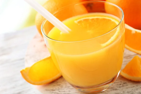 Copo de suco de laranja com palha e fatias em fundo de mesa de madeira — Fotografia de Stock