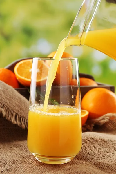 Pouring orange juice from glass carafe, on wooden table and bright background — Stock Photo, Image