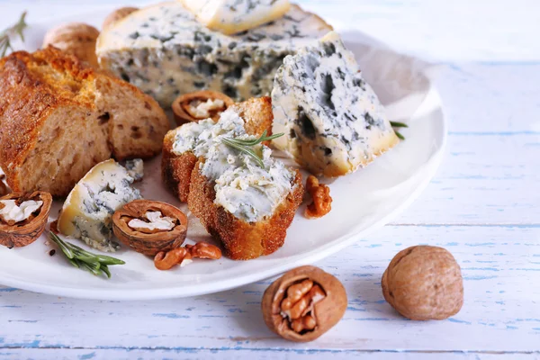 Queijo azul com raminhos de alecrim, pão e nozes na placa e cor de fundo de mesa de madeira — Fotografia de Stock