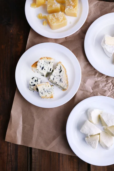 Pratos de vários tipos de queijo em folha de papel sobre fundo de mesa de madeira — Fotografia de Stock