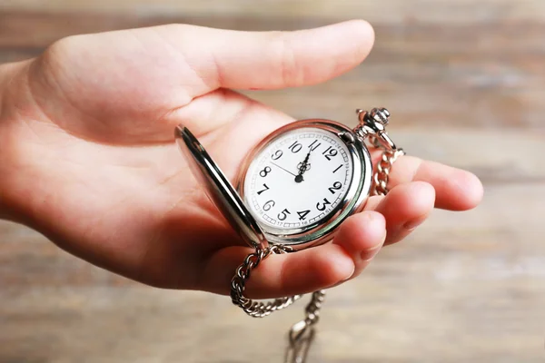 Silver pocket clock in hand on wooden background — Stock Photo, Image