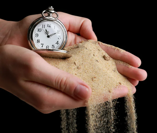 Silver pocket clock in hands and sand flowing away on black background — Stock Photo, Image