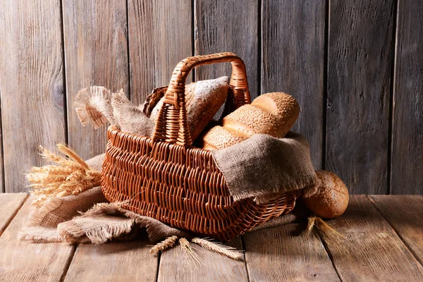 Different bread in wicker basket on table on wooden background — Stock Photo, Image