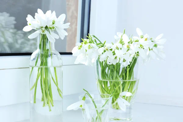 Beautiful bouquets of snowdrops in vases on windowsill — Stock Photo, Image