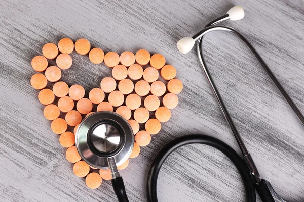 Corazón de píldoras y estetoscopio sobre fondo de madera —  Fotos de Stock