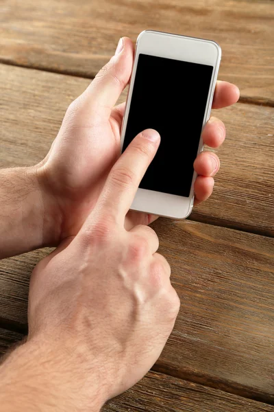 Manos sosteniendo el teléfono móvil inteligente sobre fondo de mesa de madera — Foto de Stock