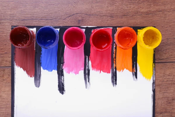 Pinceladas coloridas com latas de tinta em folha branca sobre fundo de mesa de madeira — Fotografia de Stock