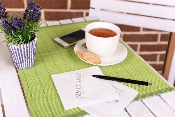 Φλιτζάνι τσάι με στυλό και επιχειρήσεων σημειώσεις σε χαρτοπετσέτα στο τραπέζι με πράσινο μπαμπού mat και τούβλο φόντο τοίχο — Φωτογραφία Αρχείου