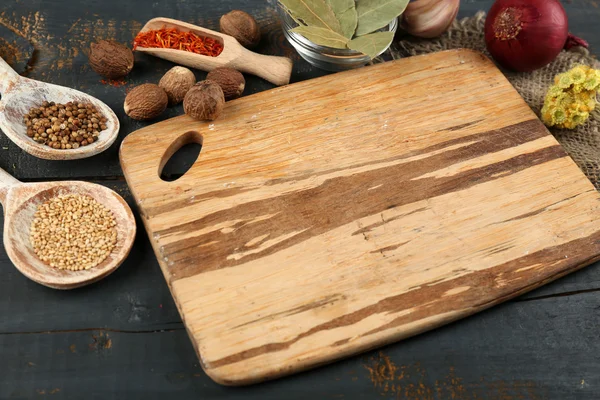 Different spices and herbs with cutting board on color wooden table background — Stock Photo, Image