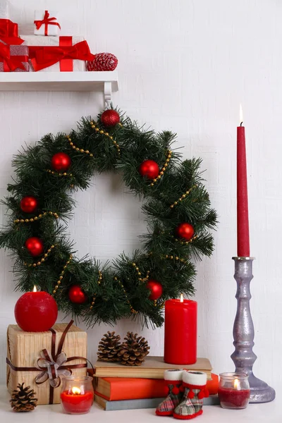 Kerstdecoratie met krans, kaarsen en huidige vakken op plank op witte muur achtergrond — Stockfoto