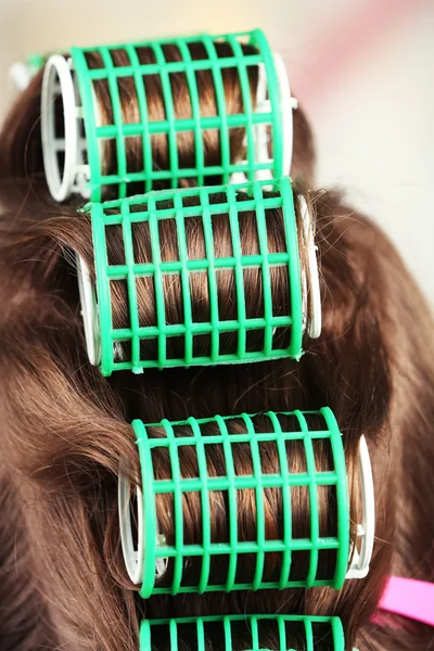 Long female hair during hair dressing with curler, close-up, on light background