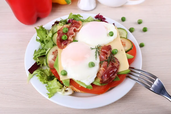 Panino con uova in camicia, pancetta e verdure su piatto su fondo di legno — Foto Stock