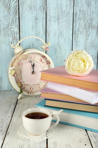 Šálek čaje s knihami a hodiny na dřevěné pozadí — Stock fotografie