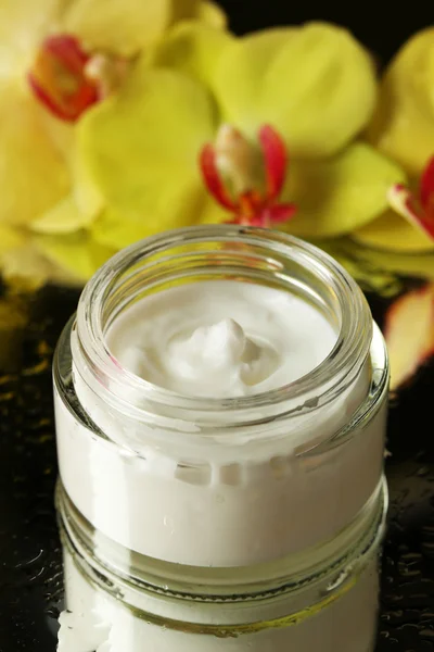 Face cream with orchid flowers on dark background — Stock Photo, Image