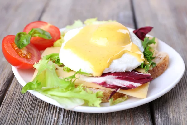 Toast with egg Benedict and tomato on plate on wooden table — Stock Photo, Image