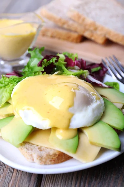 Toast with egg Benedict and avocado on plate on wooden table — Stock Photo, Image