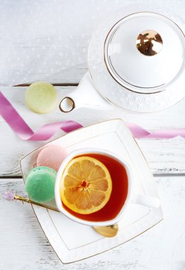 Işık arka plan üzerinde renkli tahta masada çay ile renkli macaroons