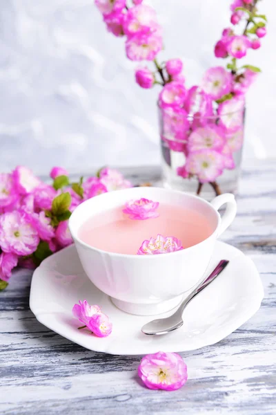 Beautiful fruit blossom with cup of tea on table on grey background — Stock Photo, Image