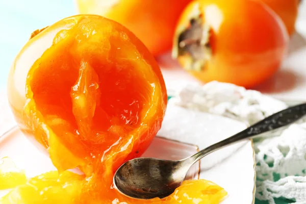 Ripe persimmons on plate, on wooden background — Stock Photo, Image