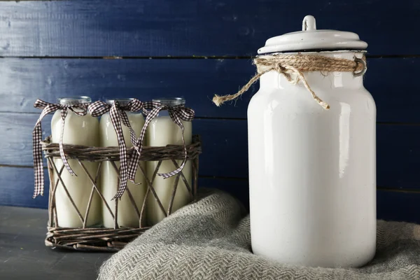 Lattina di latte e bottiglie di vetro su sfondo di legno colore — Foto Stock