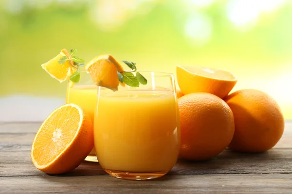 Vaso de zumo de naranja y rebanadas sobre mesa de madera y fondo brillante —  Fotos de Stock