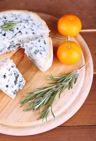 Blue cheese with sprigs of rosemary and oranges on board and wooden table background — Stock Photo, Image