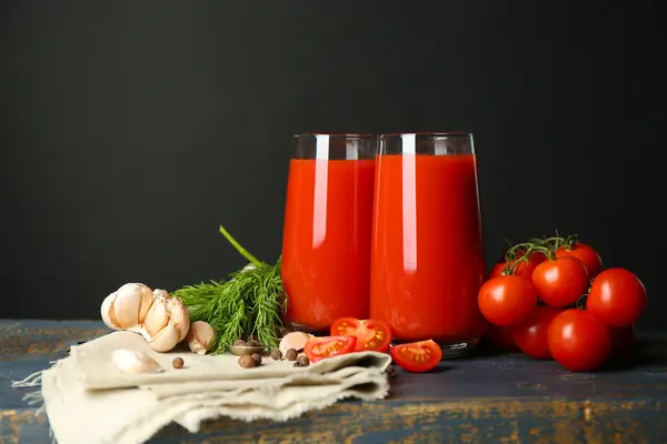 Vasos de sabroso jugo de tomate y tomates frescos sobre la mesa, sobre fondo gris —  Fotos de Stock