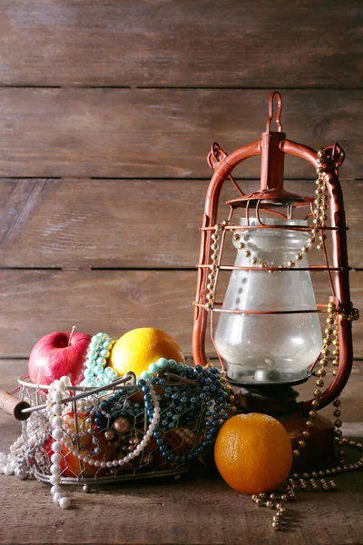 Kerosene lamp with beads and fruits on wooden planks background — Stock Photo, Image